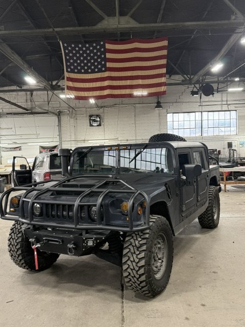 A Hummer H1 in the Classic Soft Trim shop under an American flag
